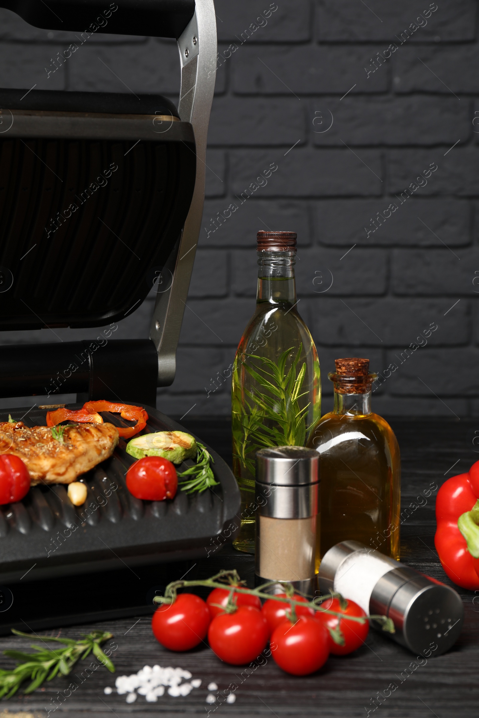 Photo of Electric grill with different products on black wooden table