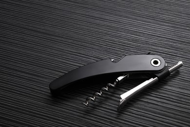 Photo of One corkscrew (sommelier knife) on black wooden table, above view