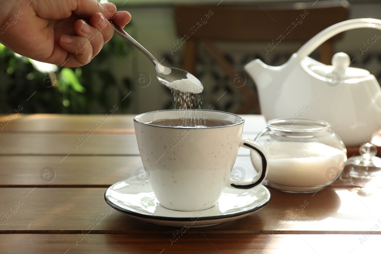 Photo of Woman adding sugar into aromatic tea at wooden table indoors, closeup