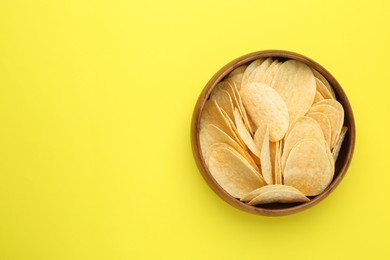 Bowl of tasty potato chips on yellow background, top view. Space for text