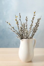 Beautiful pussy willow branches in vase on wooden table against light blue background