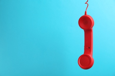 Photo of Red corded telephone handset hanging on light blue background, space for text. Hotline concept