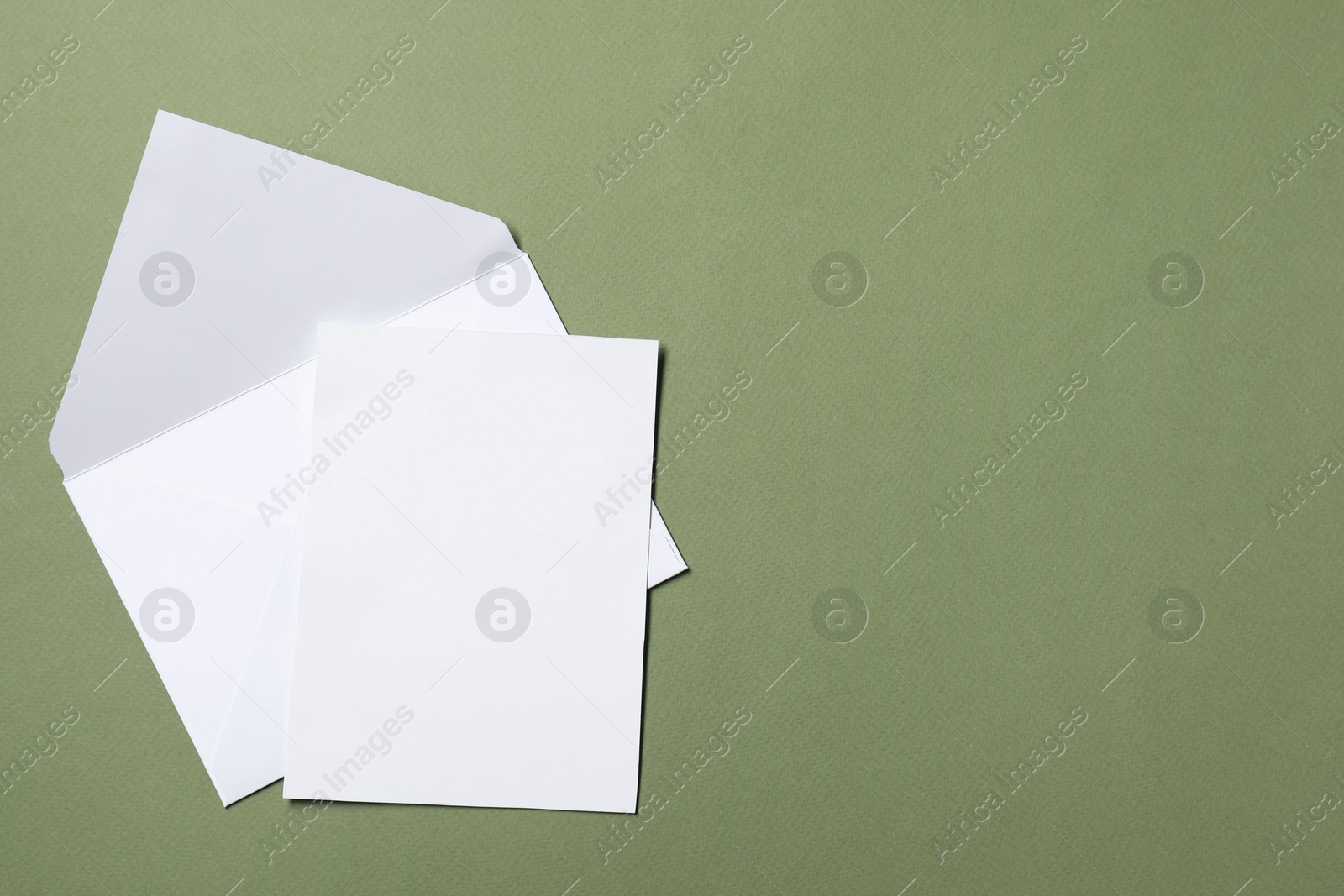Photo of Letter envelope and card on green background, top view. Space for text