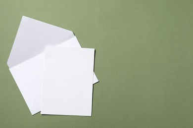 Letter envelope and card on green background, top view. Space for text