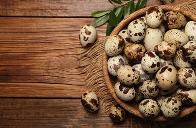 Photo of Bowl with quail eggs and green leaves on wooden table, flat lay. Space for text