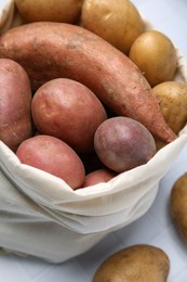Photo of Different types of fresh potatoes in bag on white table, closeup