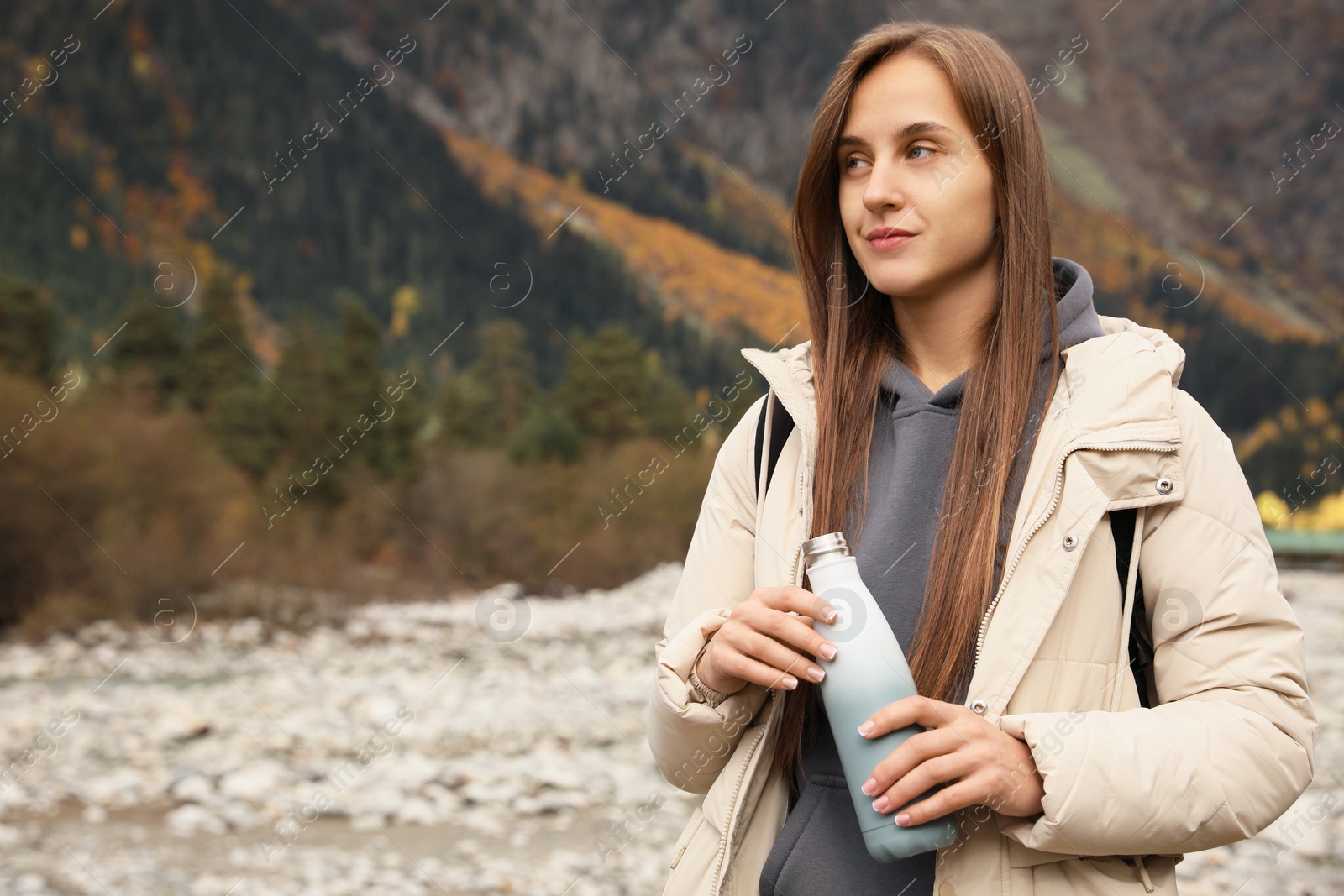 Photo of Woman holding thermo bottle with drink in beautiful mountains. Space for text