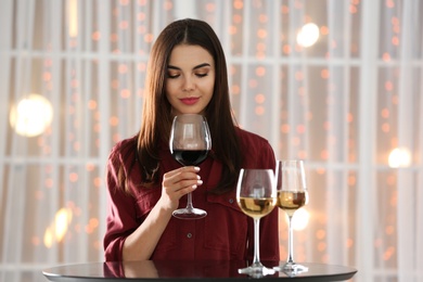 Photo of Beautiful young woman tasting luxury wine at table indoors