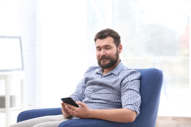Photo of Portrait of confident mature man with mobile phone in armchair