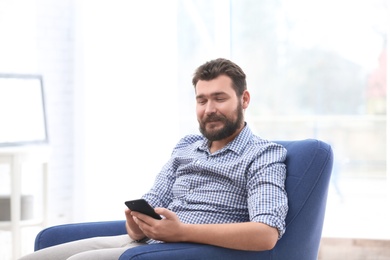 Portrait of confident mature man with mobile phone in armchair