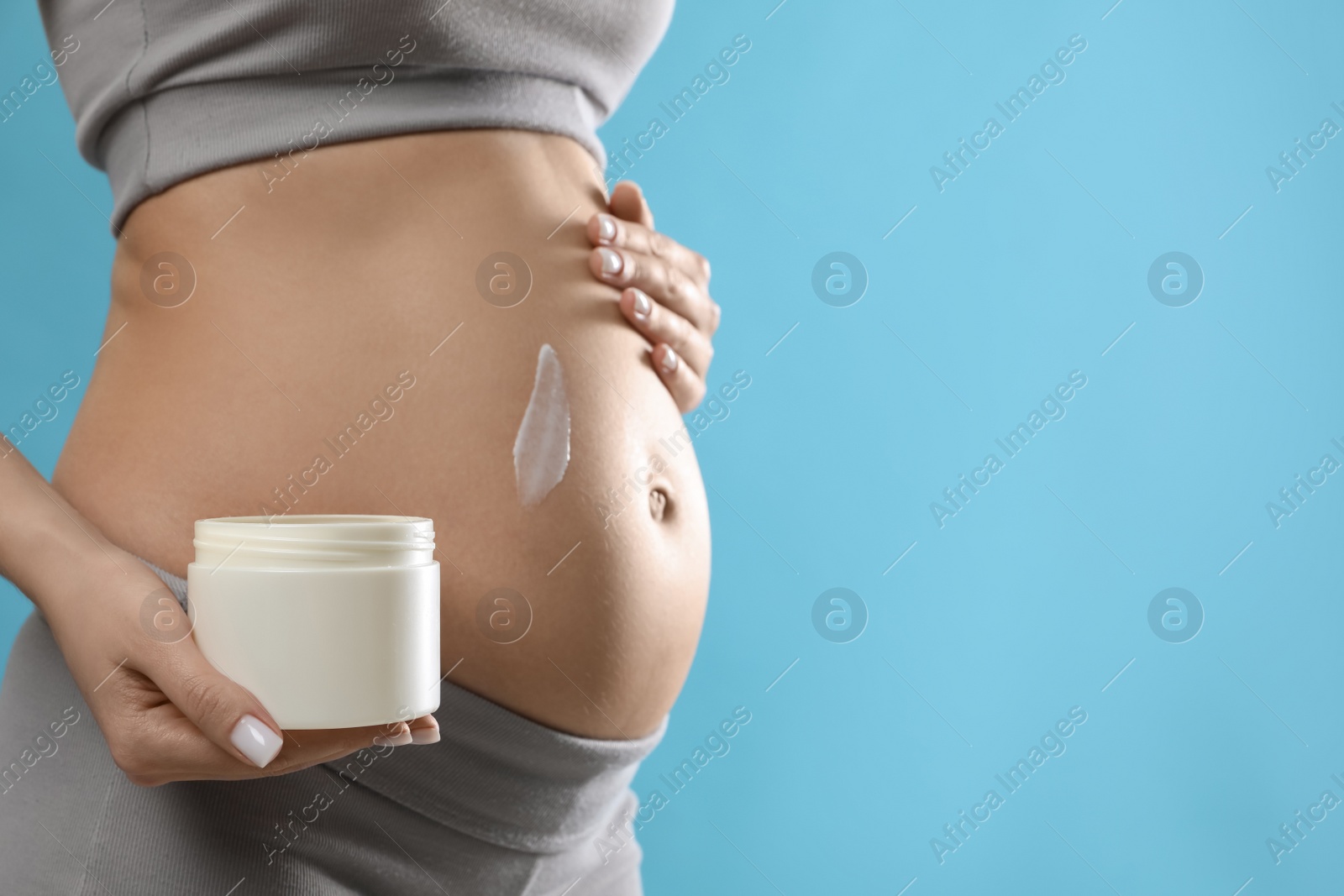 Photo of Pregnant woman with cosmetic product on light blue background, closeup. Space for text