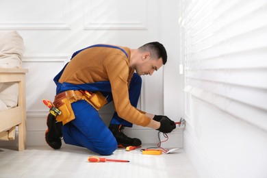 Photo of Professional electrician with tester checking voltage indoors