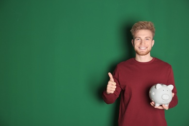 Photo of Young man with piggy bank on color background, space for text. Money saving