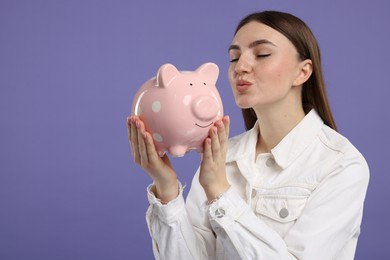 Woman with piggy bank on purple background, space for text