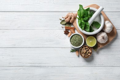 Flat lay composition with different natural spices and herbs on white wooden table, space for text
