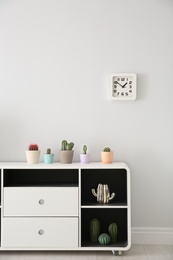 Photo of Beautiful cacti in flowerpots on white cabinet indoors