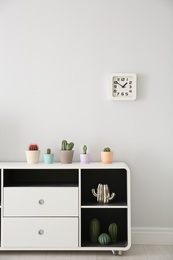 Beautiful cacti in flowerpots on white cabinet indoors