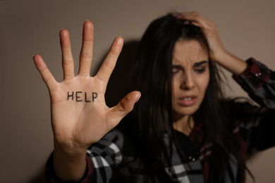 Photo of Abused young woman showing palm with word HELP near beige wall, focus on hand. Domestic violence concept