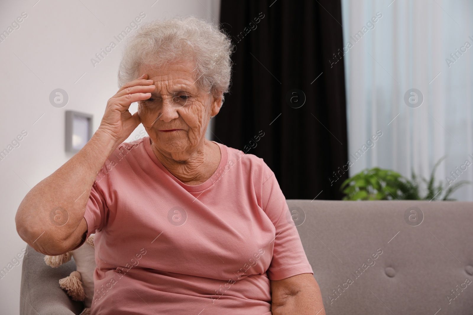 Photo of Senior woman with headache sitting on sofa at home. Space for text