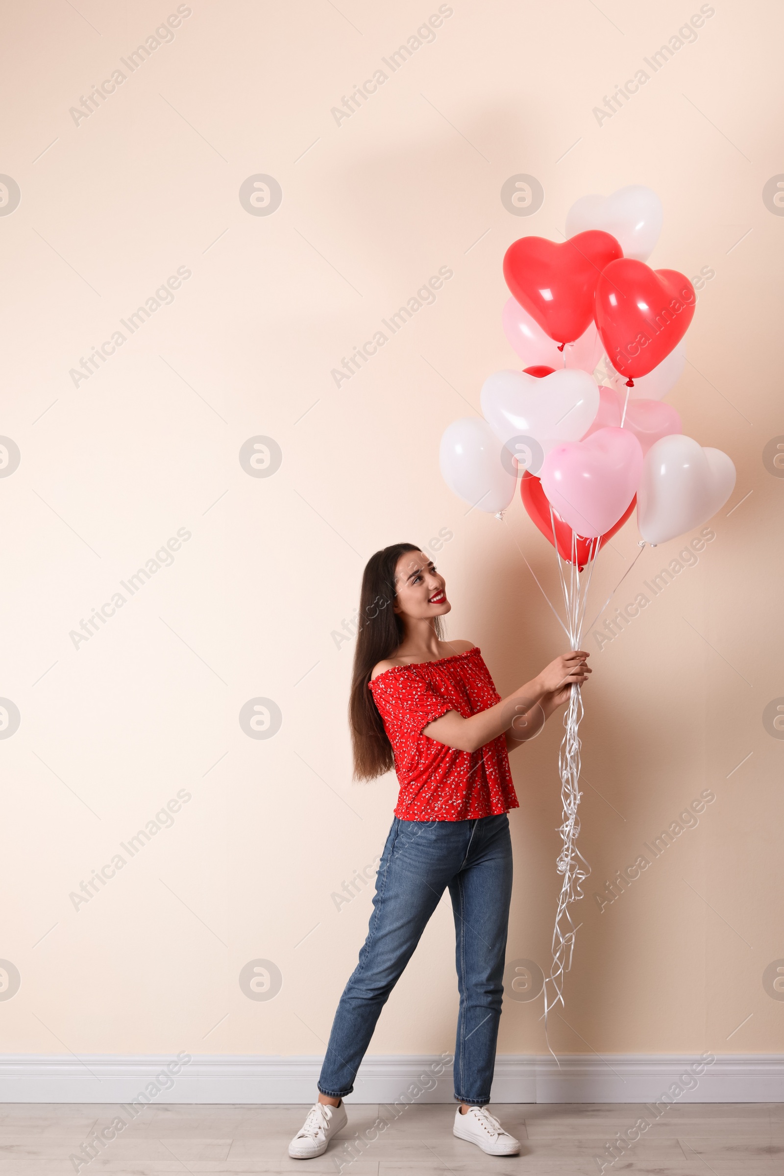 Photo of Beautiful young woman with heart shaped balloons near beige wall. Valentine's day celebration