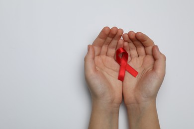 Photo of Little girl holding red ribbon on white background, top view. AIDS disease awareness
