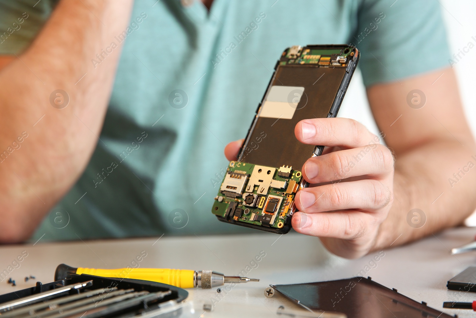 Photo of Technician with mobile phone at table in repair shop, closeup