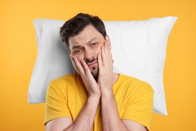 Tired man with pillow on yellow background. Insomnia problem