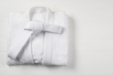Photo of White karate belt and kimono on wooden background, top view. Space for text