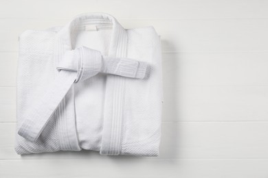 White karate belt and kimono on wooden background, top view. Space for text