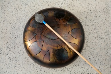 Photo of Steel tongue drum and soft mallet on grey table, top view. Percussion musical instrument