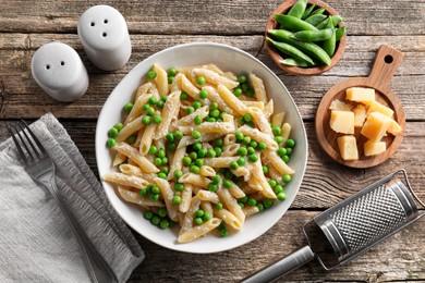 Delicious pasta with green peas, cheese, grater and fork on wooden table, top view