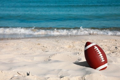 Photo of American football ball on beach. Space for text