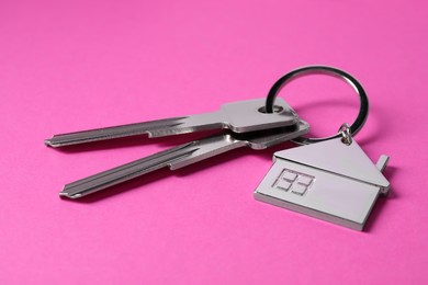 Photo of Keys with keychain in shape of house on pink background, closeup