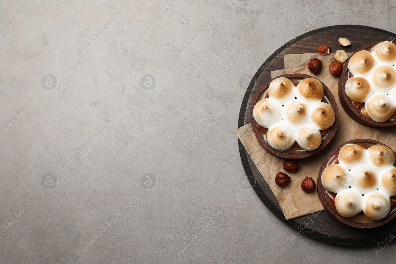 Photo of Delicious salted caramel chocolate tarts with meringue and hazelnuts on grey table, top view. Space for text