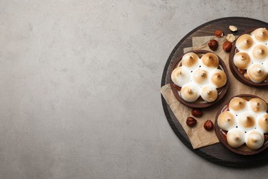 Delicious salted caramel chocolate tarts with meringue and hazelnuts on grey table, top view. Space for text