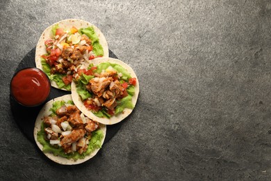 Photo of Delicious tacos with vegetables, meat and ketchup on grey textured table, top view. Space for text