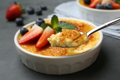 Photo of Eating delicious creme brulee with berries from spoon at grey table, closeup