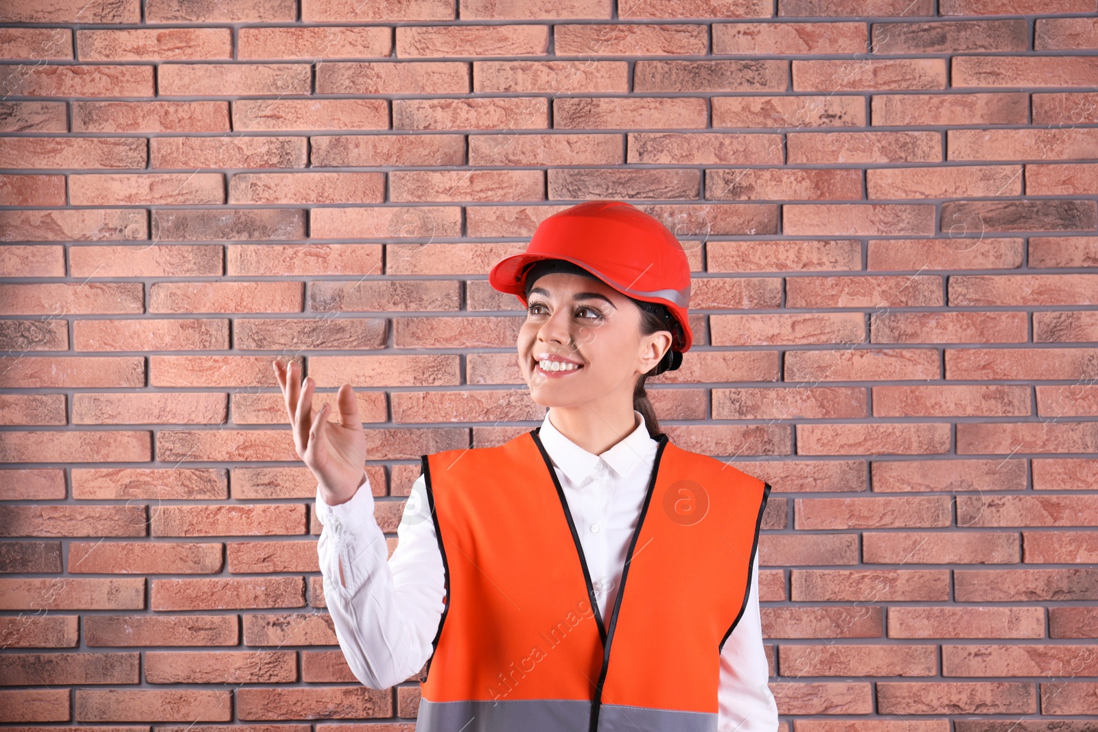 Photo of Female industrial engineer in uniform on brick wall background. Safety equipment