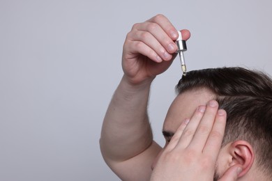 Baldness concept. Man dripping serum onto his hair on light grey background, closeup. Space for text