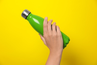 Photo of Woman holding modern green thermos on yellow background, closeup