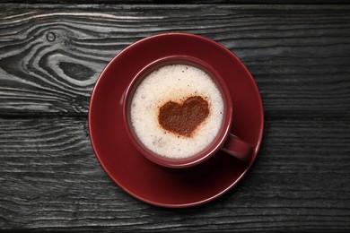 Photo of Cup of aromatic coffee with heart shaped foam on black wooden table, top view
