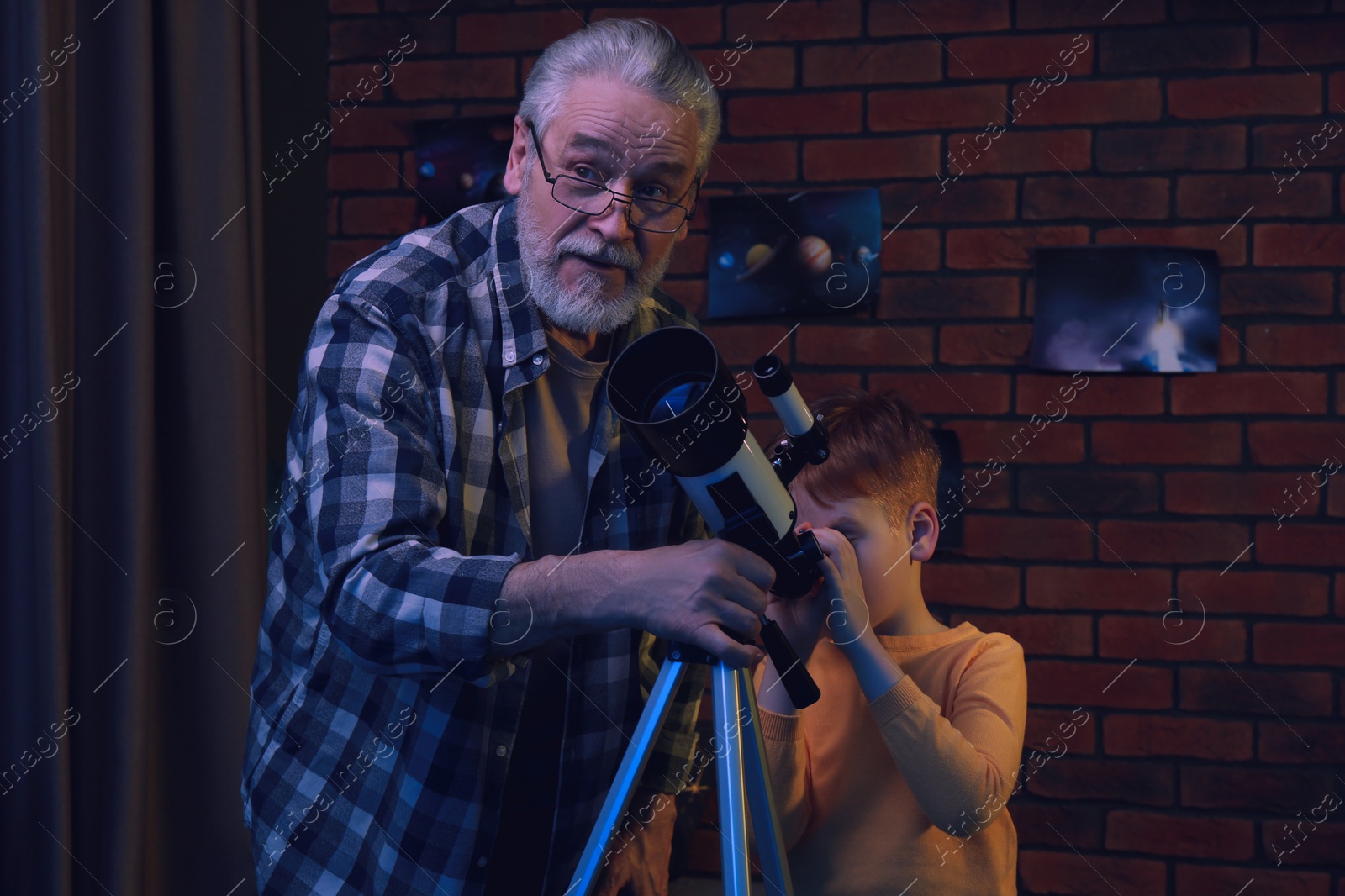 Photo of Little boy with his grandfather looking at stars through telescope in room