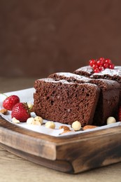 Tasty chocolate sponge cake with nuts and berries on wooden table, closeup