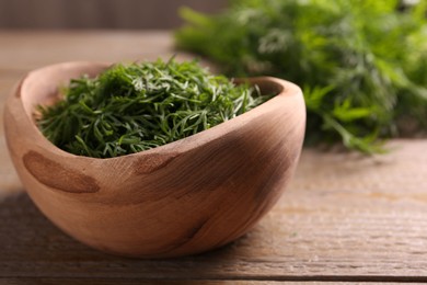 Photo of Fresh cut dill in bowl on wooden table, closeup