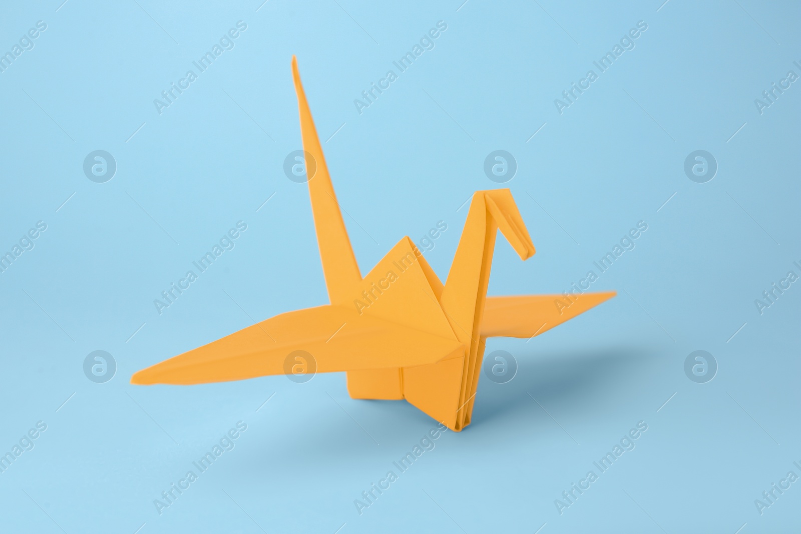 Photo of Origami art. Handmade paper crane on light blue background, closeup