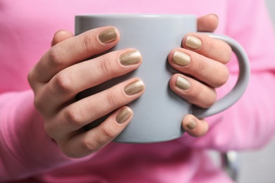 Photo of Woman with gold manicure holding cup, closeup. Nail polish trends