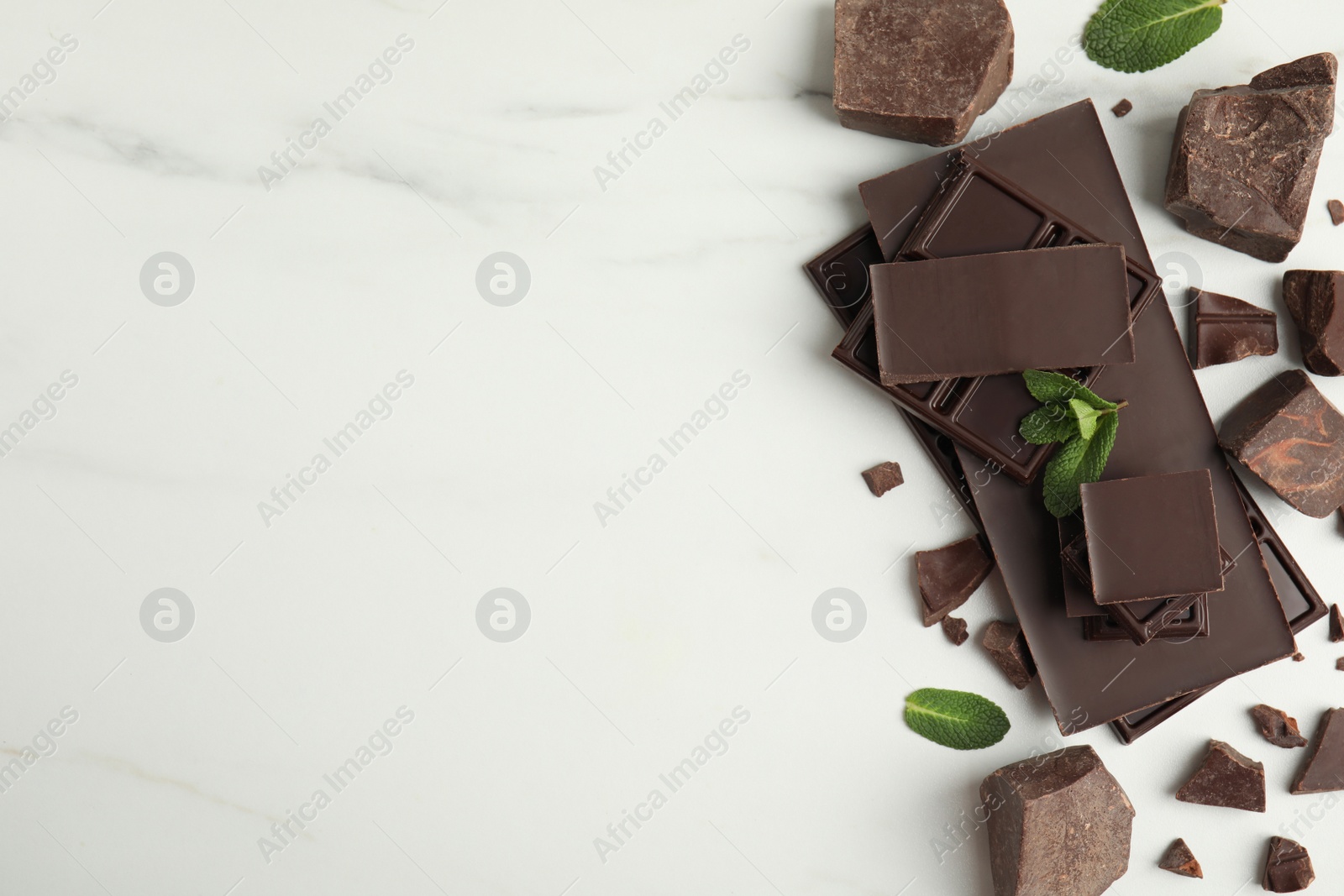 Photo of Tasty dark chocolate pieces with mint on white table, flat lay. Space for text