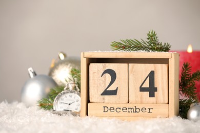 Photo of December 24 - Christmas Eve. Wooden block calendar, pocket watch and festive decor on snow