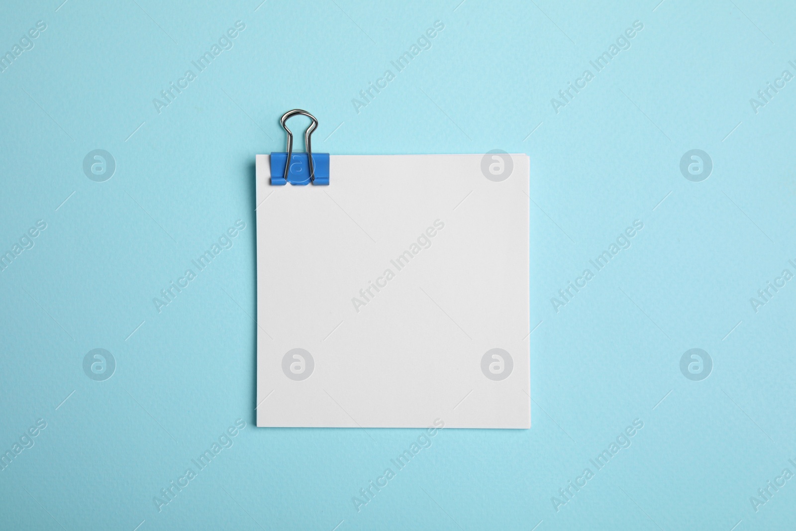 Photo of Sheet of paper with clip on light blue background, top view