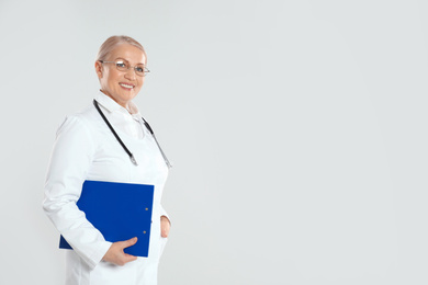 Photo of Mature doctor with clipboard on light grey background. Space for text